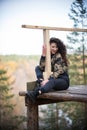 Young woman sitting on a platform on a background of the forest, smiling, hugging a rail Royalty Free Stock Photo