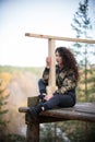 Young woman sitting on a platform on a background of the forest, smiling, hugging a rail Royalty Free Stock Photo