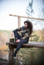 Young woman sitting on a platform on a background of the forest, smiling, hugging a rail. Chilling Royalty Free Stock Photo