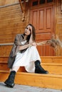 Young woman sitting on porch stairs of a wooden house with dry cereal bouquet