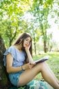 Young woman sitting and reading her favorite book on a o green gras under tree in a nice sunny summer Royalty Free Stock Photo