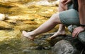 Young woman sitting on rock near forest river, cooling her feet in cold water, closeup detail Royalty Free Stock Photo