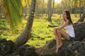 Young woman sitting on rocks in coconut trees grove, Las Galeras beach Royalty Free Stock Photo