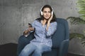 Young woman sitting in room and enjoying music streamed from mobile phone. Girl in earphones listening to songs from playlist in Royalty Free Stock Photo