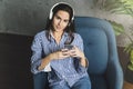 Young woman sitting in room and enjoying music streamed from mobile phone. Girl in earphones listening to songs from playlist in Royalty Free Stock Photo