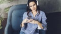Young woman sitting in room and enjoying music streamed from mobile phone. Girl in earphones listening to songs from playlist in Royalty Free Stock Photo