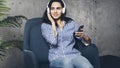 Young woman sitting in room and enjoying music streamed from mobile phone. Girl in earphones listening to songs from playlist in Royalty Free Stock Photo