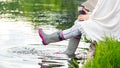 A young woman is sitting in rubber boots by the lake