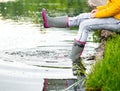 A young woman is sitting in rubber boots by the lake