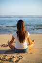 Young woman sitting on the sand in lotus pose in front of the ocean. Yoga at the beach. Hands in gyan mudra. Meditation concept.