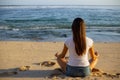 Young woman sitting on the sand in lotus pose in front of the ocean. Yoga at the beach. Hands in gyan mudra. Meditation concept.