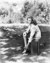 Young woman sitting on the side of the road on her suitcase, rubbing her aching feet Royalty Free Stock Photo