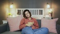 Young woman sitting on the sofa, eating popcorn, watching TV and falling alseep