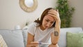 Young woman sitting on sofa holding pregnancy test looking upset at home Royalty Free Stock Photo