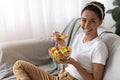 Young woman sitting on sofa at home, eating healthy food Royalty Free Stock Photo
