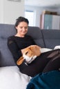 Young woman sitting on sofa and pet her beagle dog in bright room Royalty Free Stock Photo