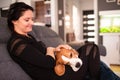 Young woman sitting on sofa and pet her beagle dog in bright room Royalty Free Stock Photo