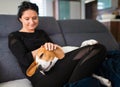 Young woman sitting on sofa and pet her beagle dog in bright room Royalty Free Stock Photo