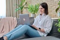 Young woman sitting on sofa using laptop for work, freelancing, learning Royalty Free Stock Photo