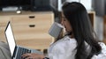 Young woman sitting on sofa and using mock up laptop computer and drinking coffee in living room. Royalty Free Stock Photo