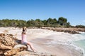 Young woman sitting on some rocks on an idyllic white sand beach on the Mediterranean coast.