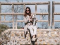 Young woman sitting on a stone fence with her Schauzer dog, poses and touches her hair looking straight ahead Royalty Free Stock Photo