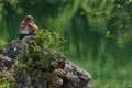 Young woman sitting on a stone on the shore of the lake Superior Fusine lake, Julian Alps, Italy, Europe.