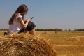 Young woman sitting on the straw bale in field