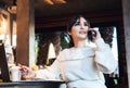 Young woman sitting at table in cafe, talking on cell phone, taking notes in notebook, working on laptop. Girl calls her friends Royalty Free Stock Photo