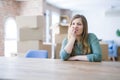 Young woman sitting on the table with cardboard boxes behind her moving to new home looking stressed and nervous with hands on Royalty Free Stock Photo