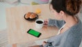 Young woman sitting at the table and drinking coffee in kitchen. Brunette girl uses smartphone, green screen. Royalty Free Stock Photo