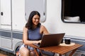 Young woman sitting at table with laptop in front of camper Royalty Free Stock Photo