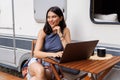 Young woman sitting at table with laptop in front of camper Royalty Free Stock Photo