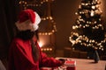 Young woman sitting table looking Christmas tree with lights illumination dreaming on Christmas Eve making a wish