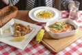 A young woman woman sitting at table with traditional Italian cuisine, lasagna, pumpkin soup with cheese and fried fish.