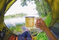 Young woman sitting in the tent and drinking tea while looking on the Desna river