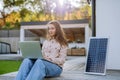 Young woman sitting on terrace, charging tablet trough solar panel.