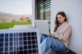 Young woman sitting on terrace, charging tablet trough solar panel.