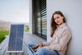 Young woman sitting on terrace, charging tablet trough solar panel.