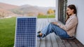 Young woman sitting on terrace, charging tablet trough solar panel.