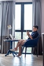 Young woman sitting and typing message on phone while working on computer during the quarantine stay Royalty Free Stock Photo