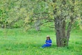 A young woman is sitting under a tree and reading a book. Girl in a blue dress with a book on a background of spring nature Royalty Free Stock Photo