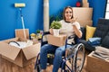 Young woman sitting on wheelchair moving to a new home pointing to the back behind with hand and thumbs up, smiling confident Royalty Free Stock Photo