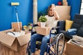 Young woman sitting on wheelchair moving to a new home surprised with hand on head for mistake, remember error