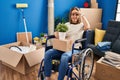 Young woman sitting on wheelchair moving to a new home very happy and smiling looking far away with hand over head Royalty Free Stock Photo