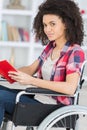 Young woman sitting in wheelchair reading book Royalty Free Stock Photo
