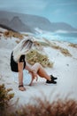 Young woman sitting on white sand dune surrounded by barren desert vegetation. Atlantic ocean coastline in background Royalty Free Stock Photo