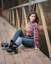 Young woman sitting whith ukulele guitar on bridge in autumn forest
