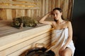 Young woman sitting on a wooden bench in a traditional sauna.