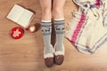 Young woman sitting on the wooden floor with cup of coffee, plaid, cookie and book. Close-up of female legs in warm socks with a d Royalty Free Stock Photo